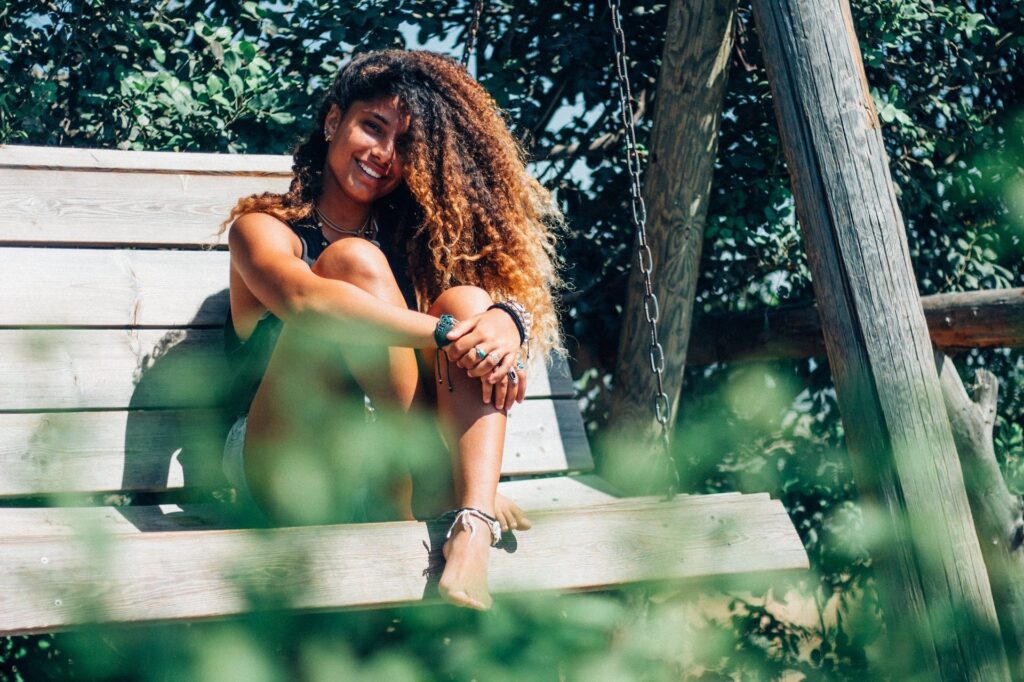 Woman sitting on swing smiling with lots of thick curly dark brown hair 