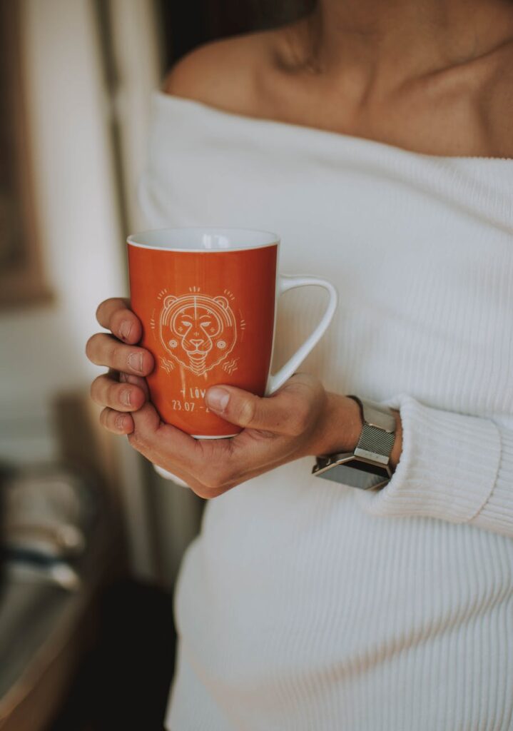 woman holding white and orange ceramic mug with leo zodiac symbol, Libra Man and Leo Woman Compatibility Chart