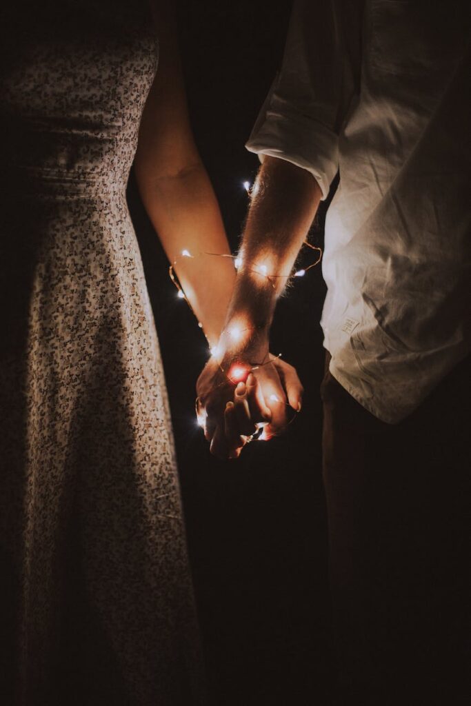 man and woman holding each others hand wrapped with string lights, Libra Man and Leo Woman Compatibility